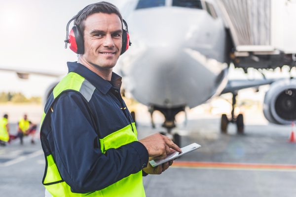 Portrait of smiling worker writing information in digital device while standing at airport
